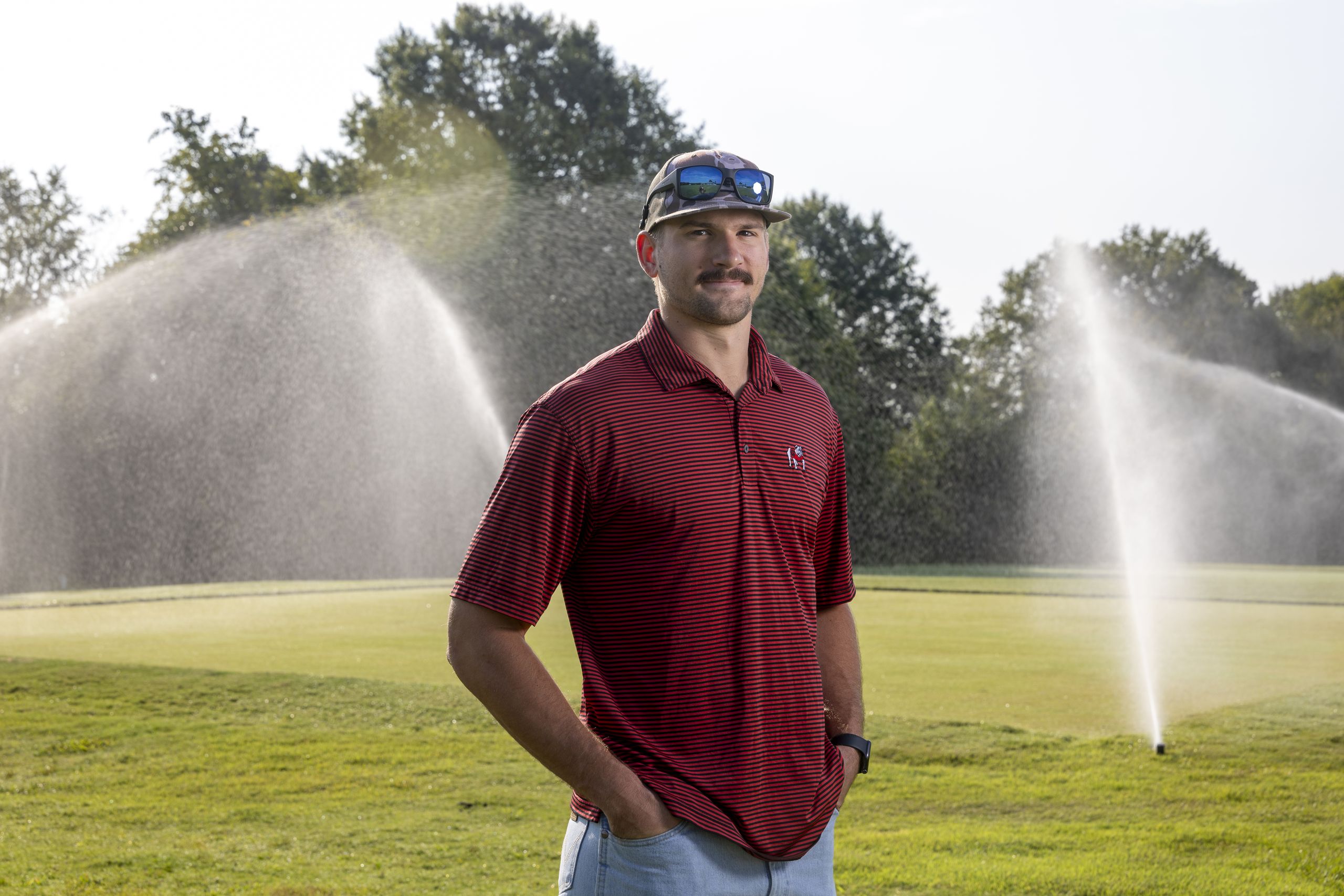 Gavin Shytle photographed in from of a patch of turf that's being sprayed by sprinklers.