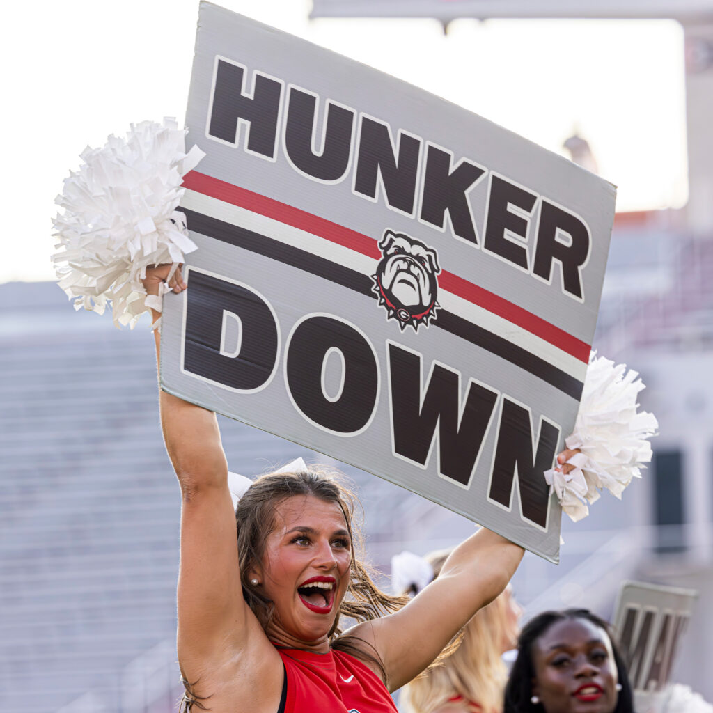 Emma Schroeder emphatically holding a sign that reads "Hunker Down" while cheering.