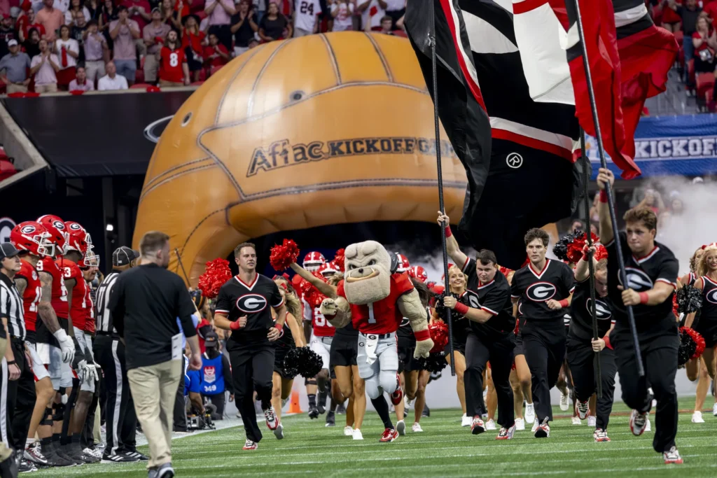 UGA's energetic mascot, Hairy Dawg, runs out onto the field ahead of the Georgia Bulldogs while fans cheer in the background.