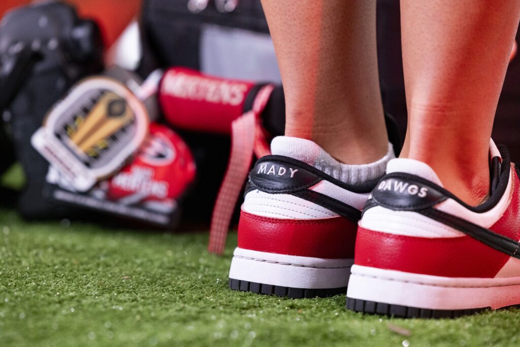 A closeup someone wearing tennis shoes with "MADY" printed on the back of one and "DAWGS" printed on the back of the other.