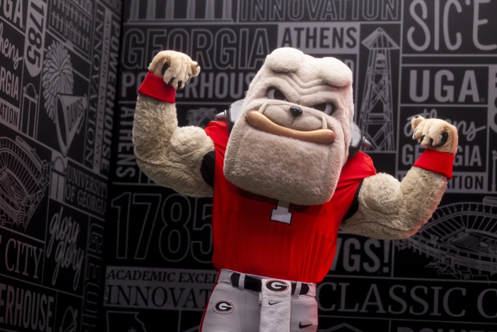 Hairy Dawg, UGA's bulldog mascot flexes his muscles in a red football jersey.