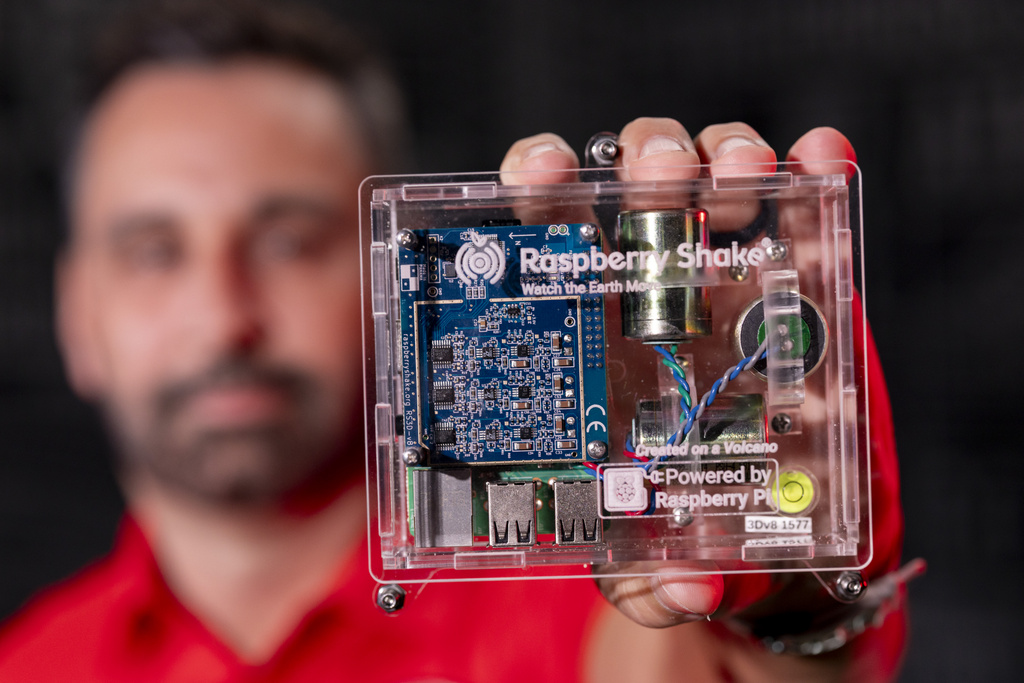 Department of Geology faculty member Adam Milewski holds up a phone-sized raspberry shake seismograph.