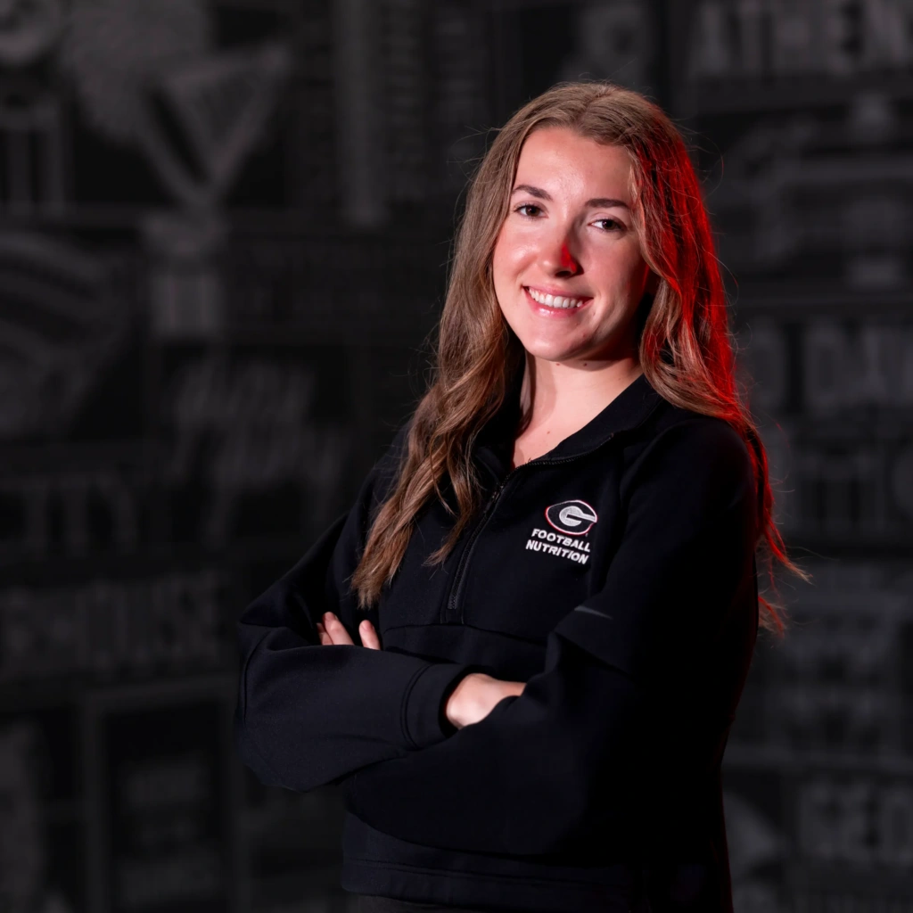 A young woman wearing athletic clothing poses with her arms crossed.